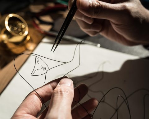 Zelfgemaakte ring van koperdraad met een kleine kraal, liggend op een houten ondergrond